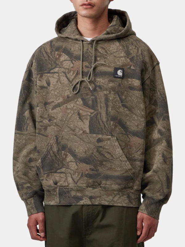 Tan camo pullover hoodie worn with hood down, model front view with chest patch logo