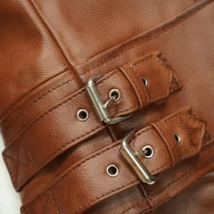 Close-up of brown leather jacket with silver buckle straps and stitching details.