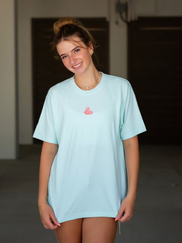 Seafoam mint cotton tee with coral embroidered logo, casual walking pose