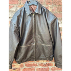 Brown leather zip-up jacket with collar and pockets hanging on brick wall