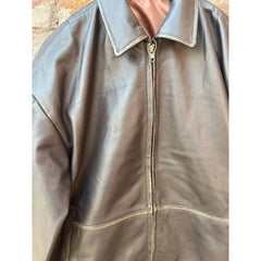 Brown leather jacket with zip front and classic collar, close-up view on textured wall