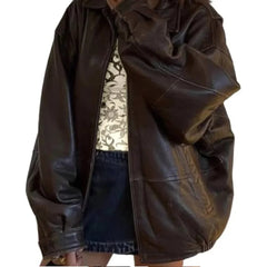 Oversized brown leather jacket styled with floral top and denim mini skirt, streetwear fashion.