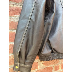Close-up of black leather jacket sleeve with button cuff and elastic hem against brick wall