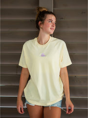Pale yellow oversized tee with embroidered logo, indoor shutter backdrop