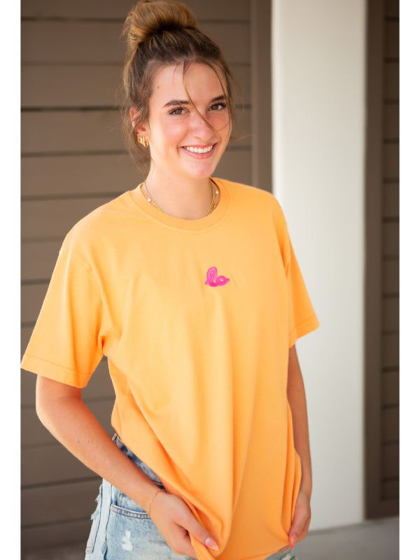 Coral orange streetwear tee with embroidered logo, outdoor wood paneling backdrop