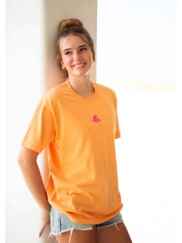 Coral orange tee with pink heart embroidered logo, outdoor daylight